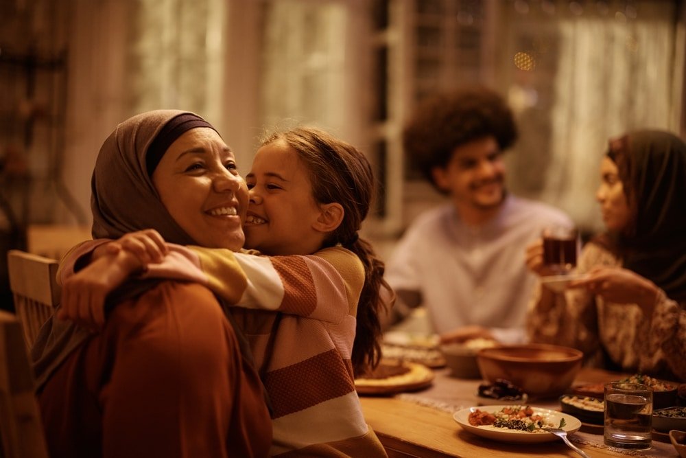 Affectionate,Muslim,Grandmother,And,Granddaughter,Embracing,During,Family,Meal,In